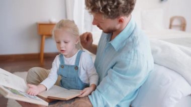Evde kitap okuyan konsantre sarışın baba ve kız.
