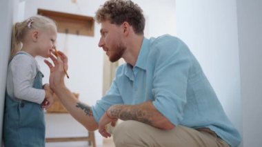 Mutlu sarışın baba evde kızının yüzüne bir şeyler çiziyor.