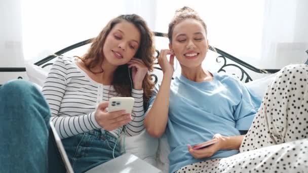 Encantadoras Novias Escribiendo Los Teléfonos Escuchando Música Los Auriculares Cama — Vídeos de Stock