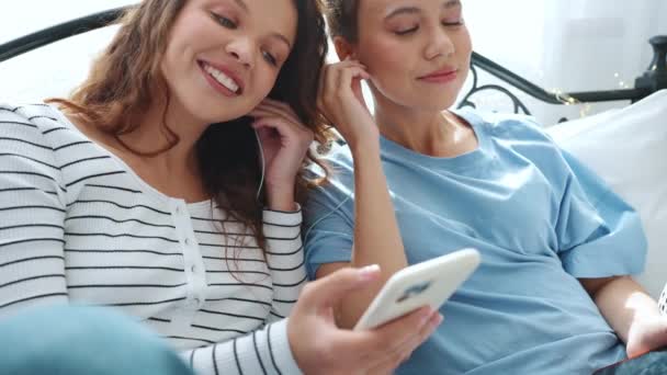 Csinos Barátnők Nézik Mobilt Zenét Hallgatnak Fülhallgatóban Ágyon — Stock videók