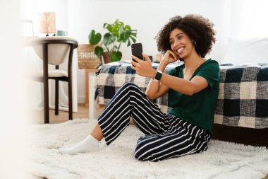 Afro kıvırcık saçlı, gülümseyen ve cep telefonuyla konuşan Afro-Amerikalı genç bir kadın.