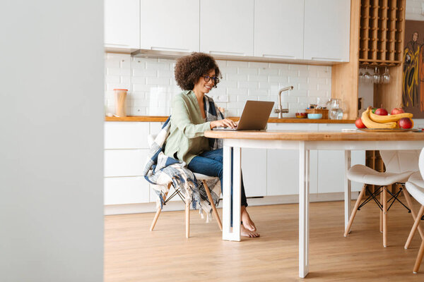 African american young woman with curly afro hairstyle and eyeglasses using laptop at home
