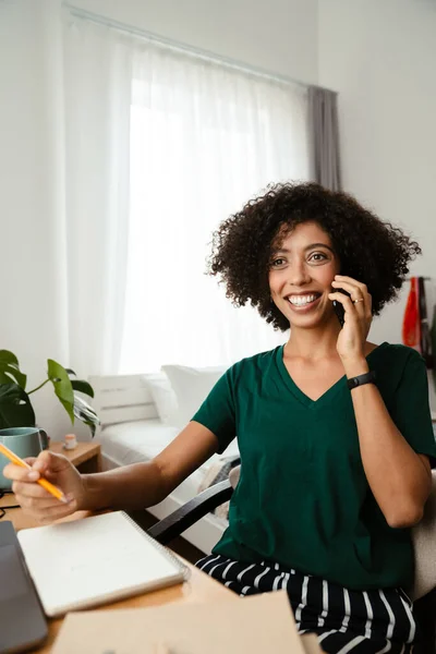 非洲裔美国妇女一边用手机交谈 一边在家里画素描本 — 图库照片