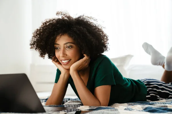 头发卷曲的非洲裔美国女青年躺在床上 在家里用笔记本电脑 — 图库照片