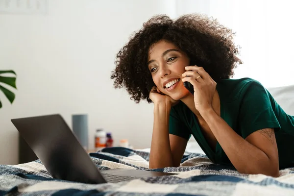 非洲裔美国妇女 头发卷曲 用手机聊天 在家里用笔记本电脑 — 图库照片