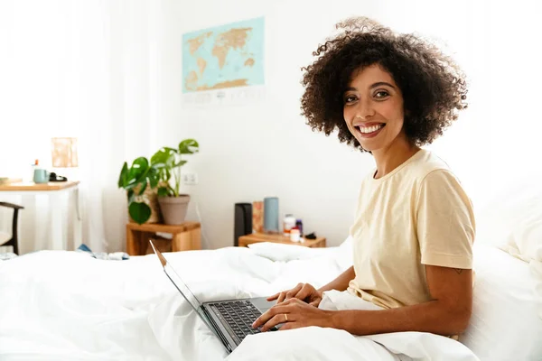 아프리카 미국인젊은 곱슬머리로 침대에 집에서 노트북을 사용하는 — 스톡 사진