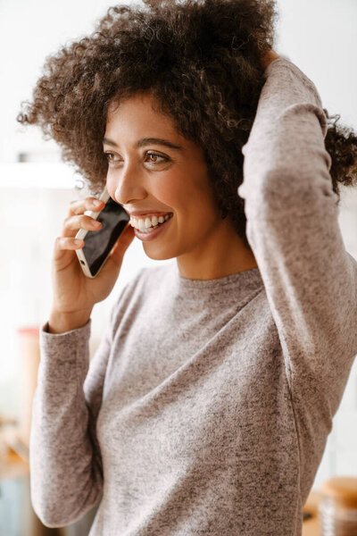 African american young woman with curly afro hairstyle smiling while using cellphone at home