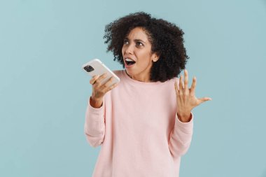 Genç İspanyol kadın mavi arka planda izole bir şekilde cep telefonuyla konuşurken el kol hareketi yapıyor