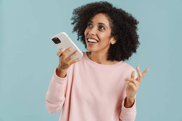 青い背景の上に隔離された携帯電話で話している間に若いヒスパニック系の女性の笑顔 — ストック写真