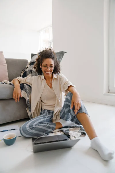 Evde Yerde Otururken Dizüstü Bilgisayar Kullanan Kıvırcık Saçlı Afrikalı Amerikalı — Stok fotoğraf
