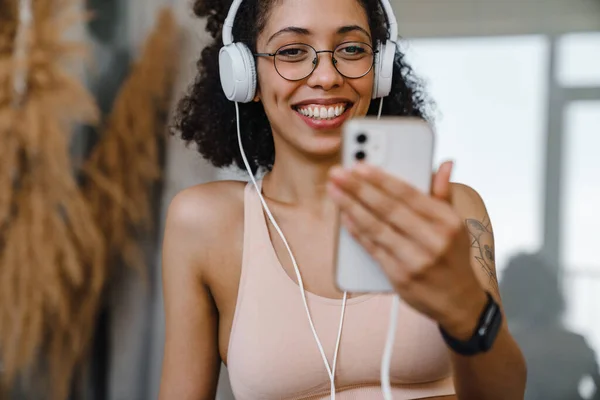 Black Young Woman Wearing Eyeglasses Using Cellphone Headphones Workout Home — Stock Photo, Image