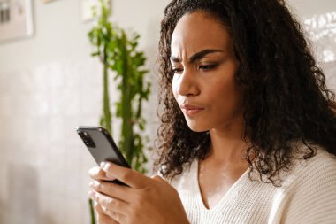 Kafede kaşlarını çatan ve cep telefonu kullanan genç siyahi kadın.