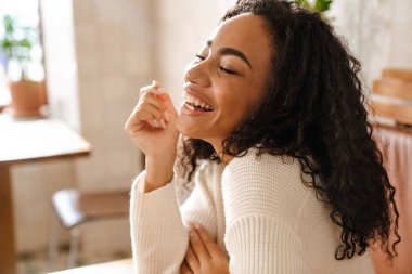 Genç siyahi kadın kafede otururken gülüyor.