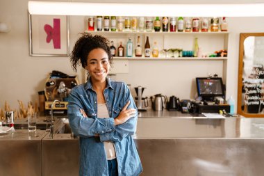 Kapalı bir kafede çalışırken gülümseyen siyah bir garson kız.