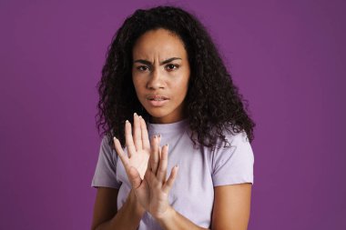 Mor arka planda izole edilmiş dur hareketi yaparken kaşlarını çatan genç siyahi kadın.