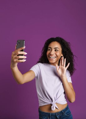 Mor arka planda izole edilmiş cep telefonuyla selfie çeken genç siyahi kadın.