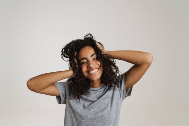 Genç siyah kadın, dalgalı saçlarıyla gülüyor ve başını beyaz arka planda tutuyor.