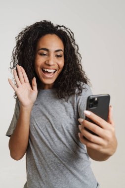 Genç siyahi kadın cep telefonu kullanıyor ve işaret dilini beyaz arka planda izole ediyor.