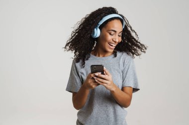 Genç siyahi kadın müzik dinlerken beyaz arka planda izole edilmiş cep telefonu kullanıyor.