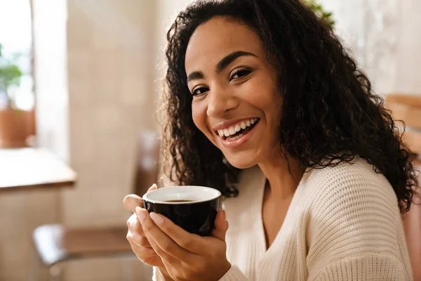 年轻的黑人妇女坐在室内咖啡店边喝咖啡边笑 — 图库照片