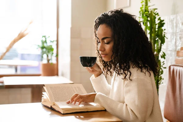 年轻的黑人妇女在室内喝咖啡和看书 — 图库照片