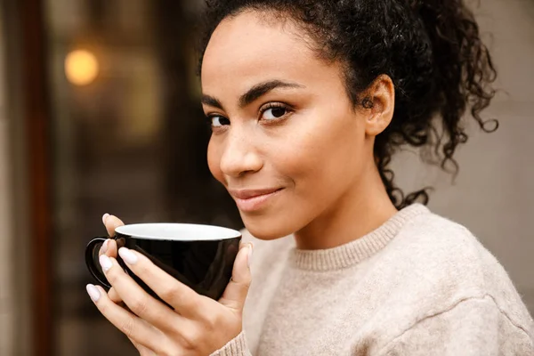 年轻的黑人妇女在外面的咖啡馆里微笑着喝咖啡 — 图库照片