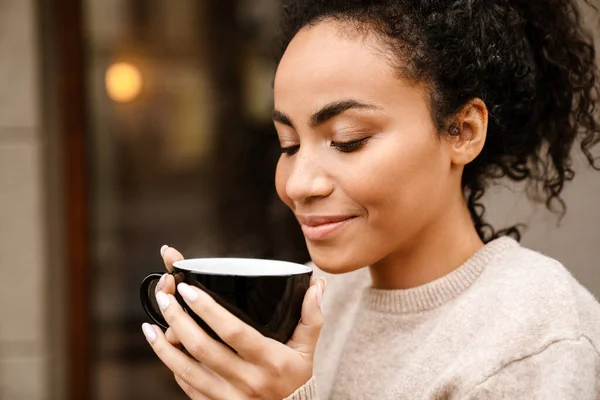 Young black woman smiling and drinking coffee in cafe outdoors