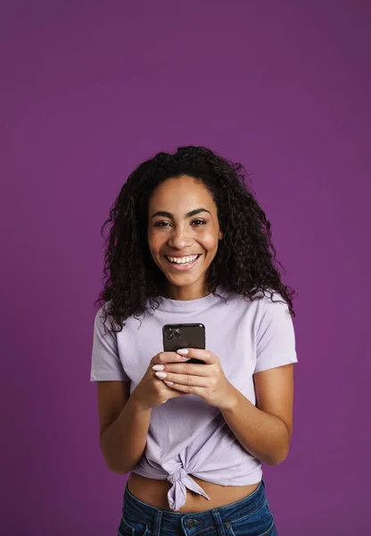 Молодая Черная Женщина Используя Мобильный Телефон Смеясь Изолированы Фиолетовом Фоне — стоковое фото