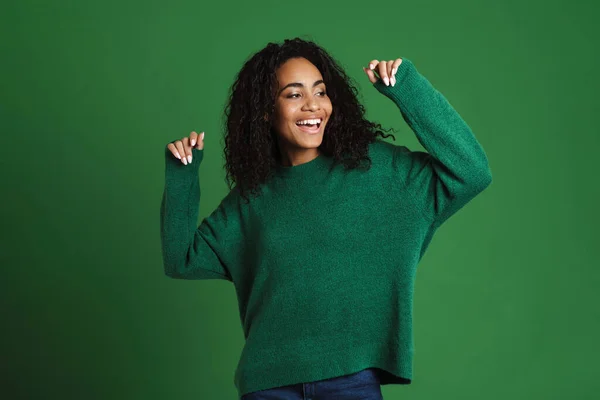 Young black woman with wavy hair smiling and dancing isolated over green background