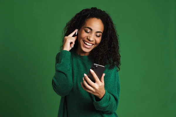 stock image Young black woman using mobile phone while listening music isolated over green background