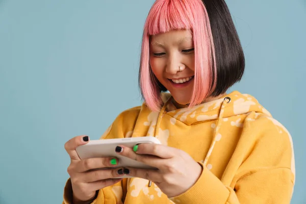 亚洲女孩 粉色头发 在手机上玩在线游戏 背景是蓝色的 — 图库照片