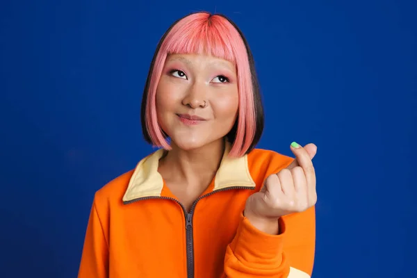 アジアの女の子とともにピンクの髪笑いながら彼女の指をこすります絶縁上の青の背景 — ストック写真