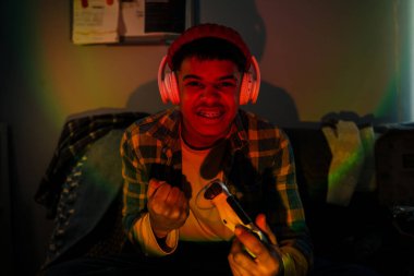 Evde video oyunu oynarken kulaklık ve kumanda kullanan Ortadoğulu genç çocuk.