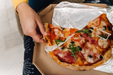 Evdeki kanepede otururken pizza yiyen genç çocuk.