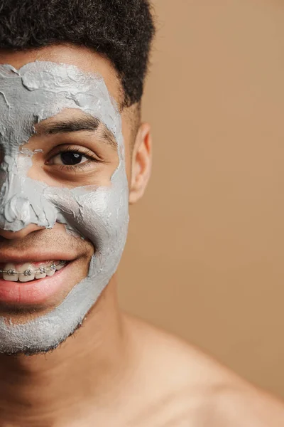 stock image Young shirtless man with cosmetic clay mask smiling at camera isolated over beige background