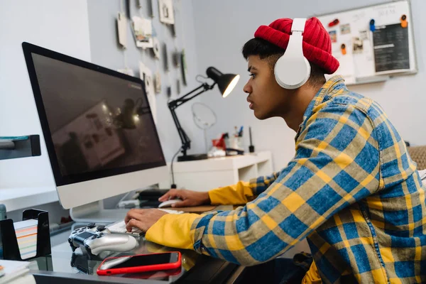 stock image Teenage boy with headphones playing video game on desktop computer at home