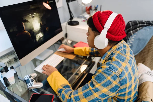 stock image Teenage boy with headphones playing video game on desktop computer at home