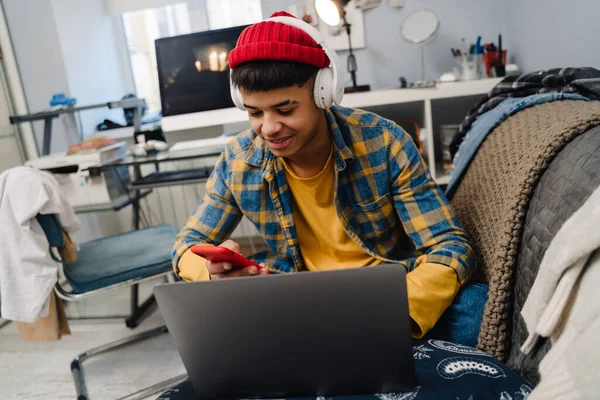 Middle Eastern Teenage Boy Using Laptop Cellphone While Sitting Couch — Stock Photo, Image
