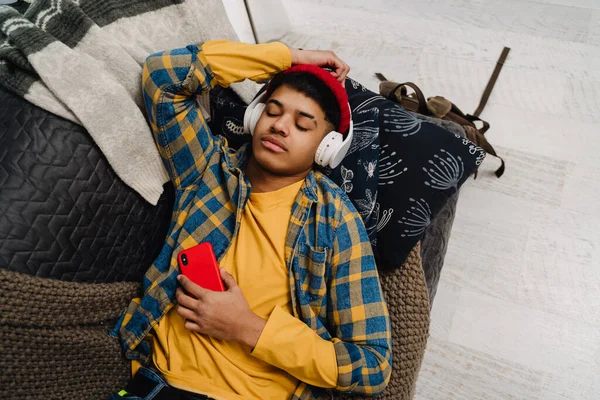 Bliskowschodni Nastolatek Korzystający Słuchawek Telefonu Komórkowego Leżącego Kanapie Domu — Zdjęcie stockowe