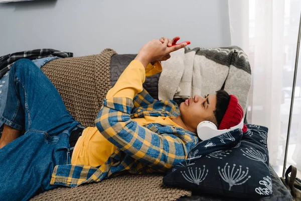 Middle Eastern Teenage Boy Using Headphones Cellphone While Lying Couch — Stock Photo, Image