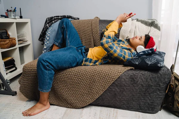 Middle Eastern Teenage Boy Using Headphones Cellphone While Lying Couch — Stock Photo, Image