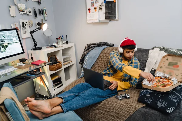 Middle Eastern Teenage Boy Eating Pizza Using Laptop While Sitting — Stock Photo, Image