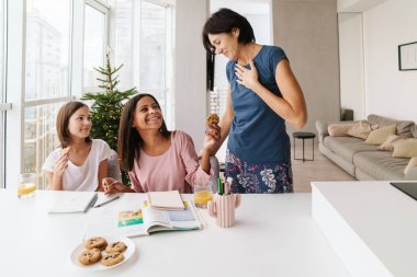 Çok ırklı kız kardeşler anneleriyle evde vakit geçirirken birlikte ödev yapıyorlar.