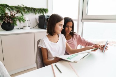 Evde birlikte ödev yaparken cep telefonu kullanan çok ırklı kız kardeşler.