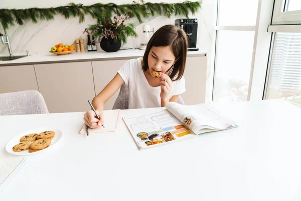 Λευκό Preteen Κορίτσι Τρώει Μπισκότο Ενώ Κάνει Την Εργασία Στο — Φωτογραφία Αρχείου
