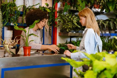 Afro-Amerikalı çiçekçi kız çiçekçide bayan müşteriyle çalışıyor.