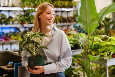 Çiçekçide çalışırken elinde saksı saksısı tutan güzel bir kız.