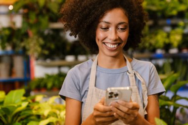 Çiçekçide saksıda çalışırken cep telefonu kullanan mutlu bir genç kız.