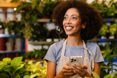 Çiçekçide saksıda çalışırken cep telefonu kullanan mutlu bir genç kız.