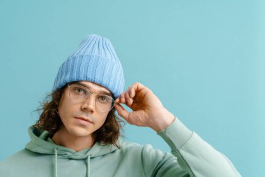 Uzun saçlı, uzun saçlı, gözlüklü, kameraya bakan ve izole edilmiş mavi arka planda duran yakışıklı bir adamın portresi.